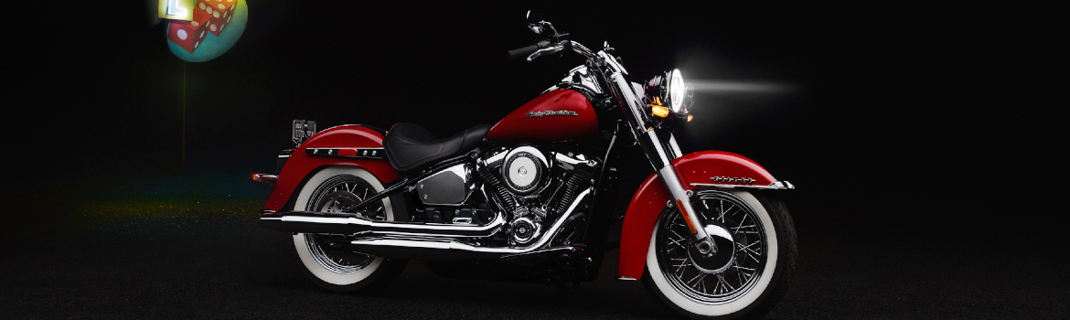 A red Harley-Davidson® Deluxe parked in a dark lot with a gambling billboard behind it.